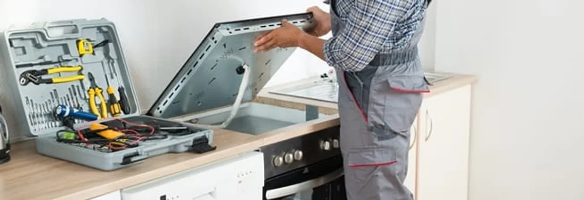 Cooktop repair technician lifting a built-in stovetop for service in Rockford, IL