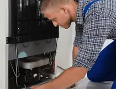 Refrigerator repair technician servicing the compressor and condenser area in Rockford, IL