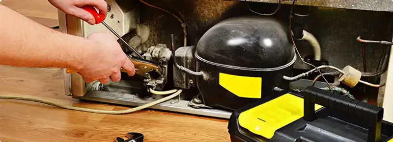 Refrigerator repair technician fixing the compressor and wiring in Rockford, IL